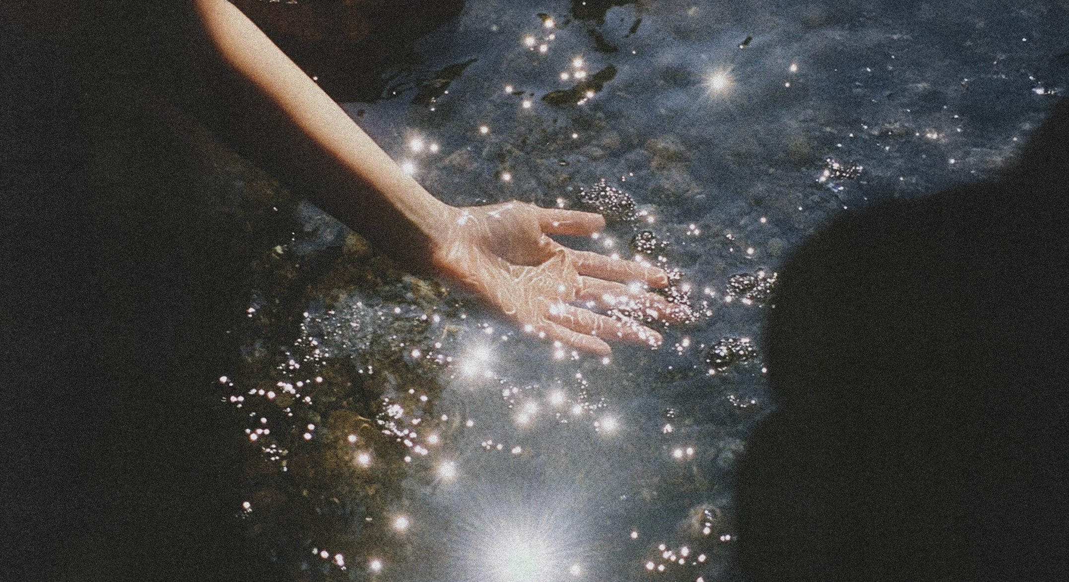Hand reaching into water with a starry effect