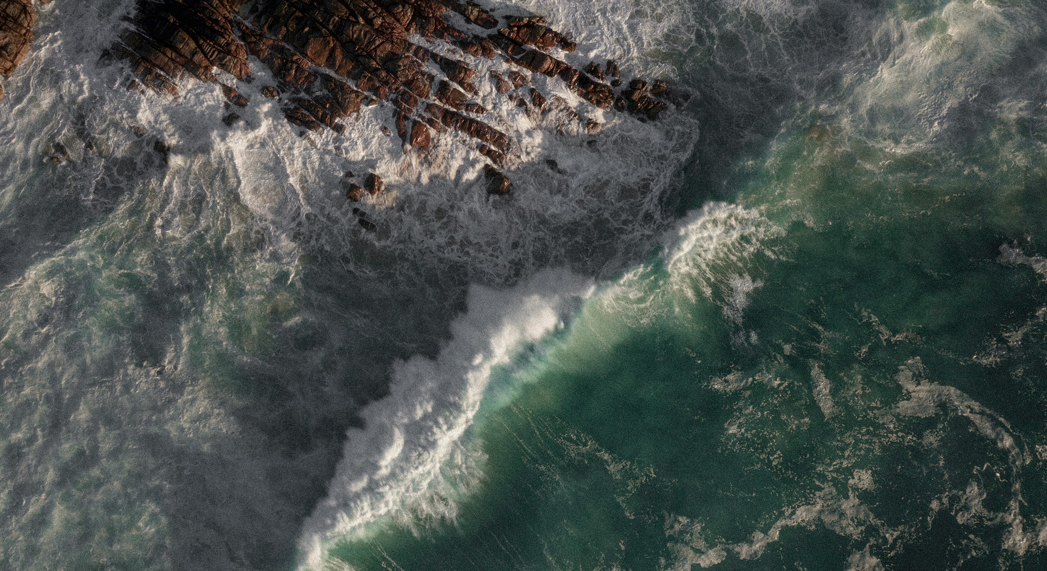 Aerial view of waves crashing against a rocky coastline.