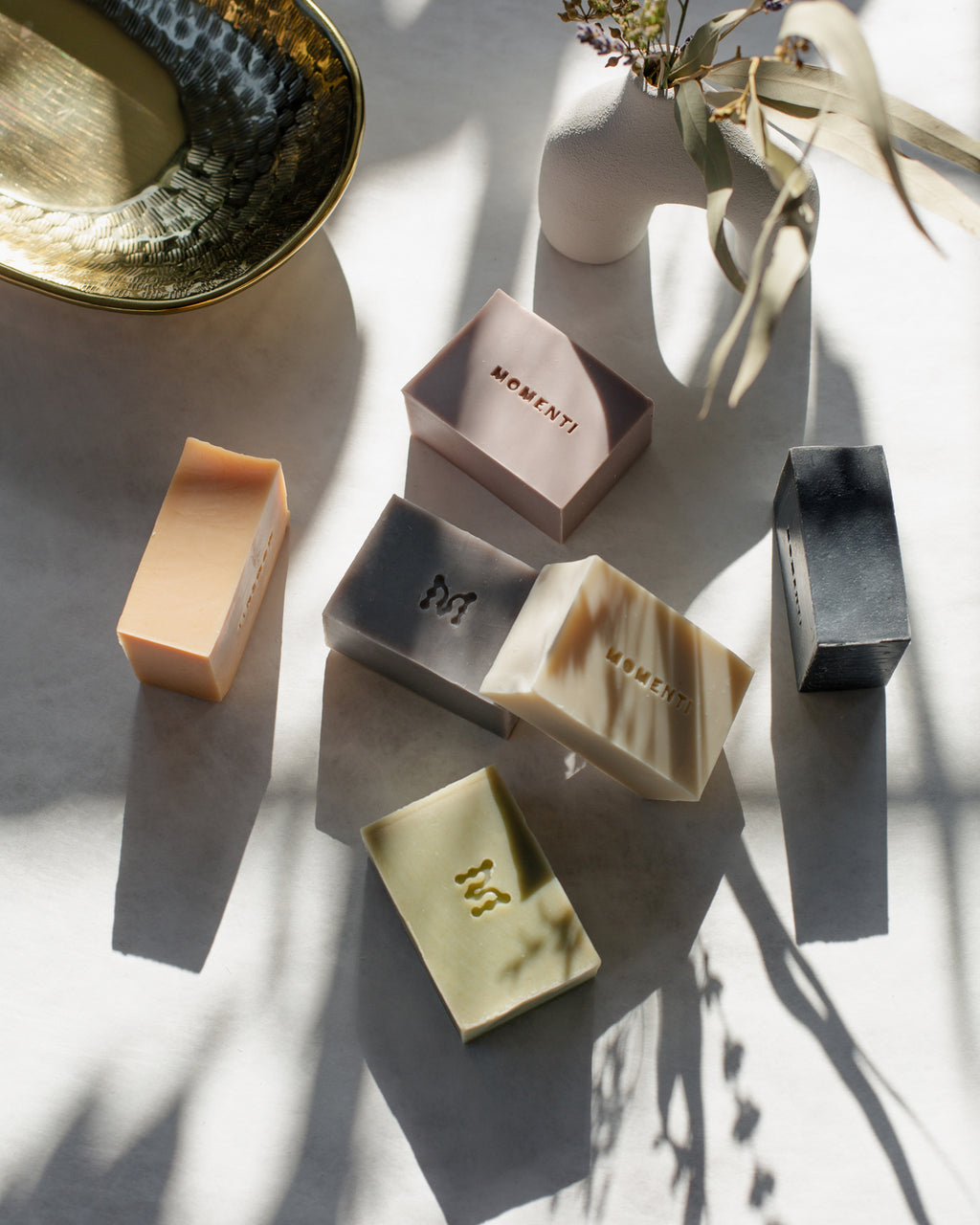 Various soaps in different shapes and colors on a light surface with 'Momenti' branding.