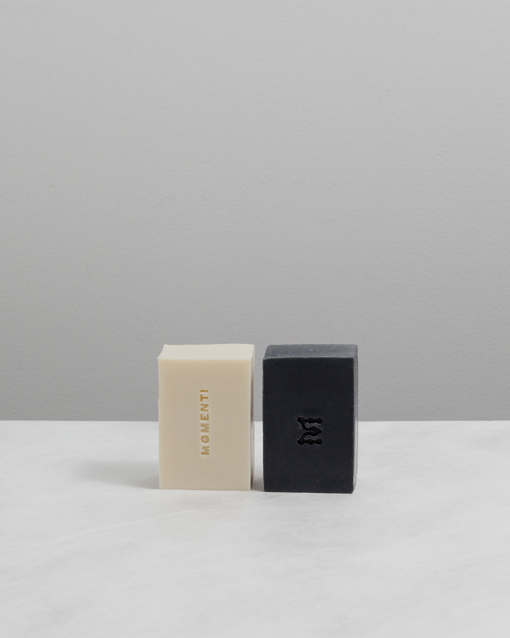 Two bars of soap, one beige and one black, on a light gray background.