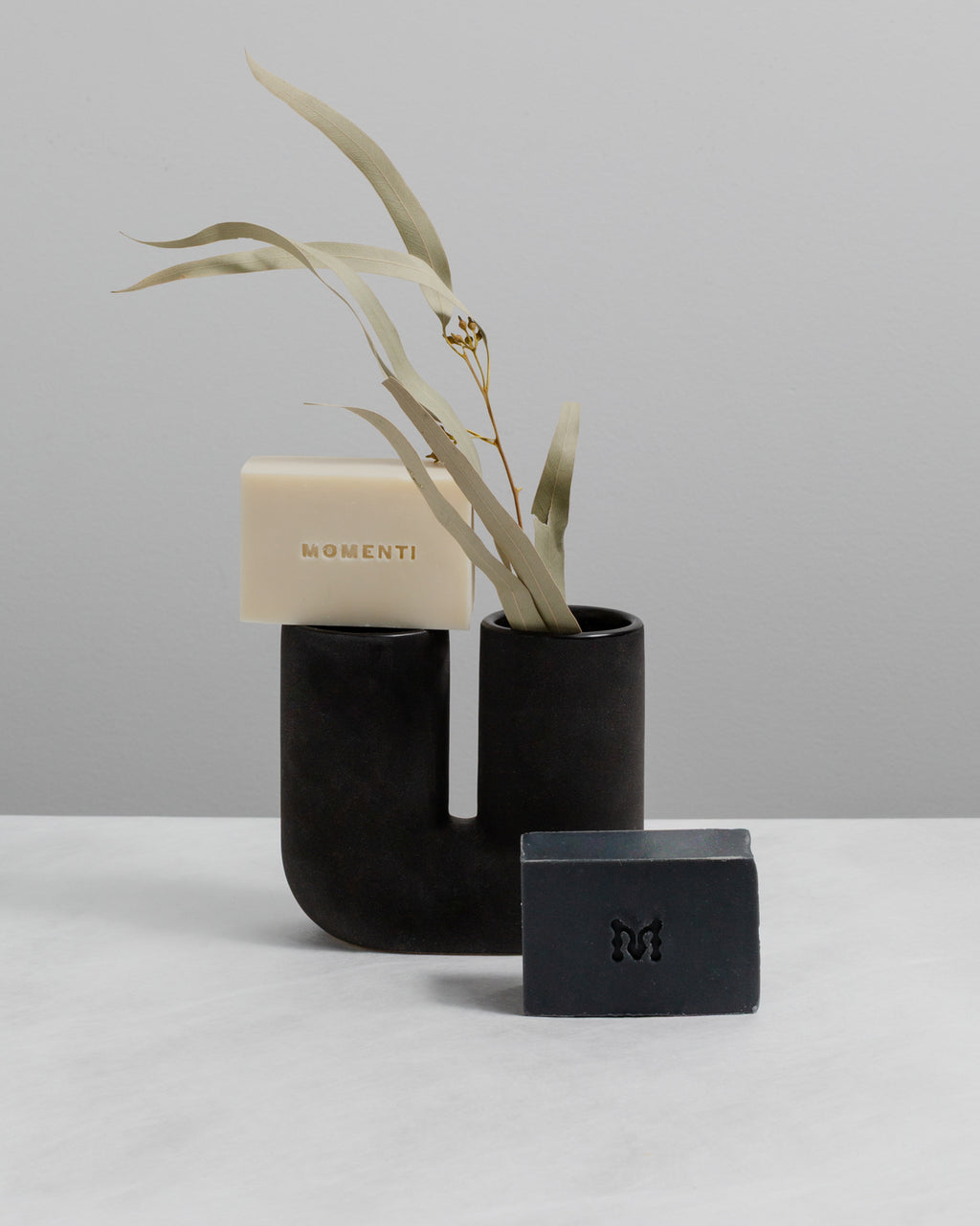 Bar of soap with a plant and black containers on a light gray background