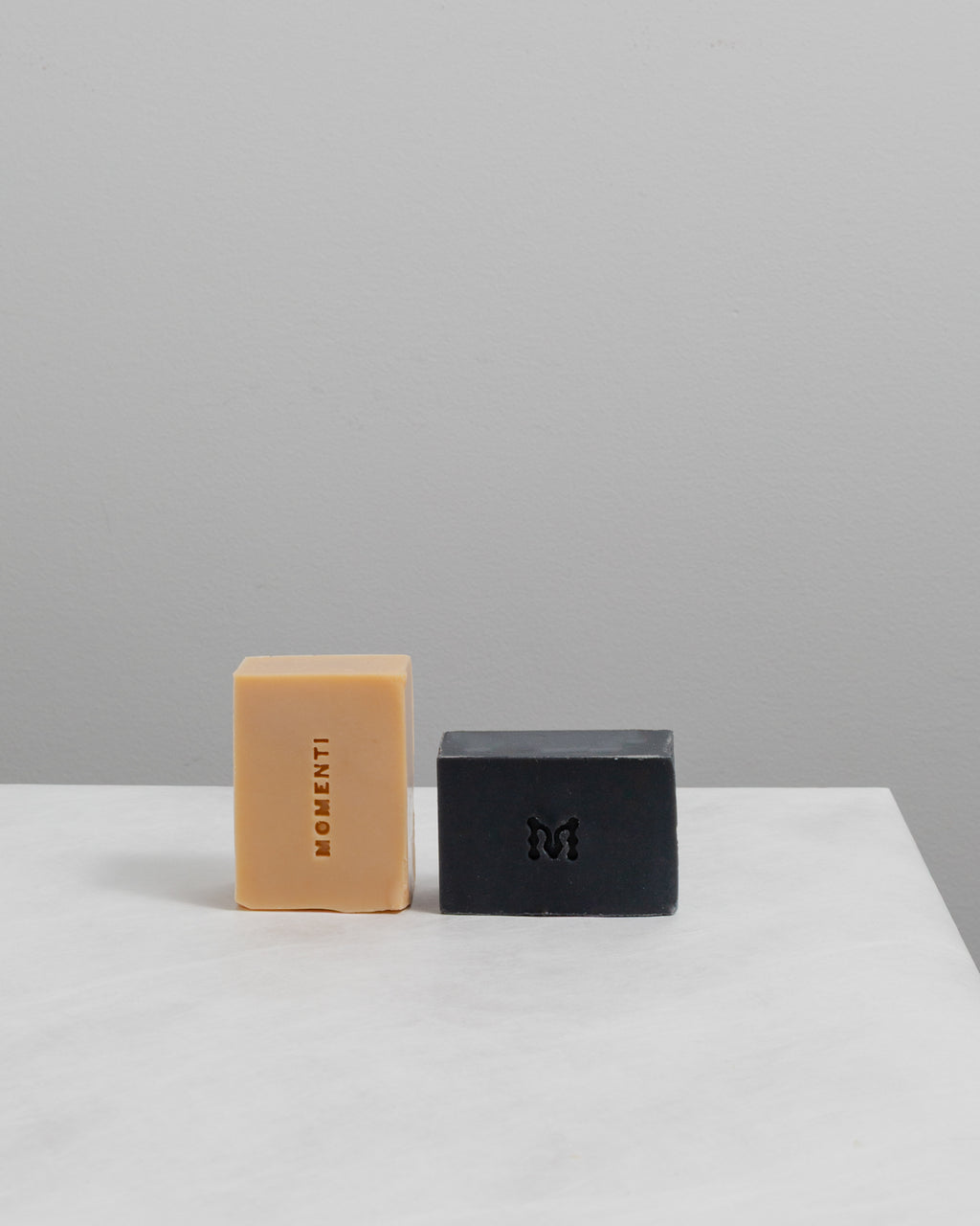 Two soap bars, one orange and one black, on a white surface with a gray background.