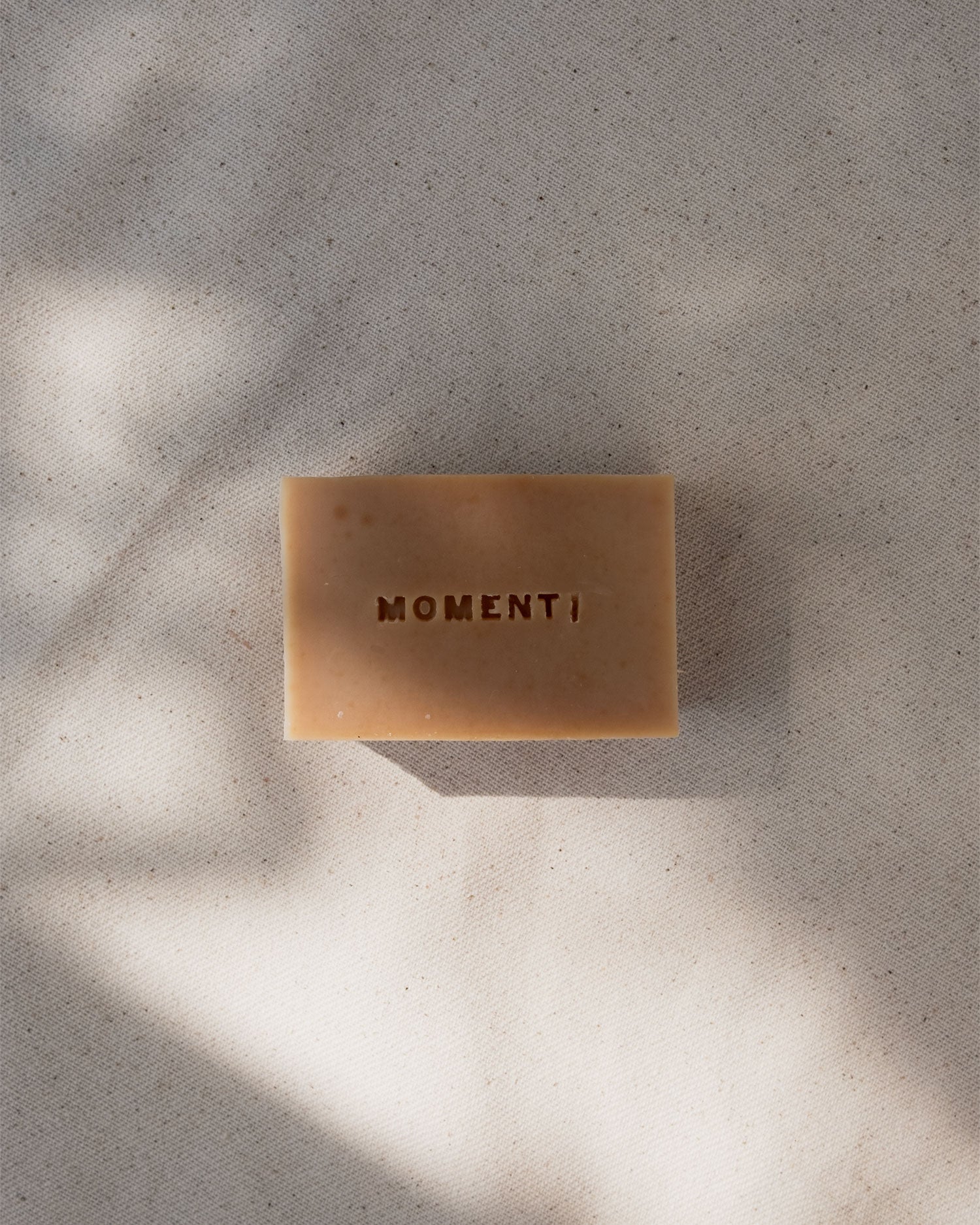 Honey bar of soap with 'MOMENTI' branding on a textured surface.