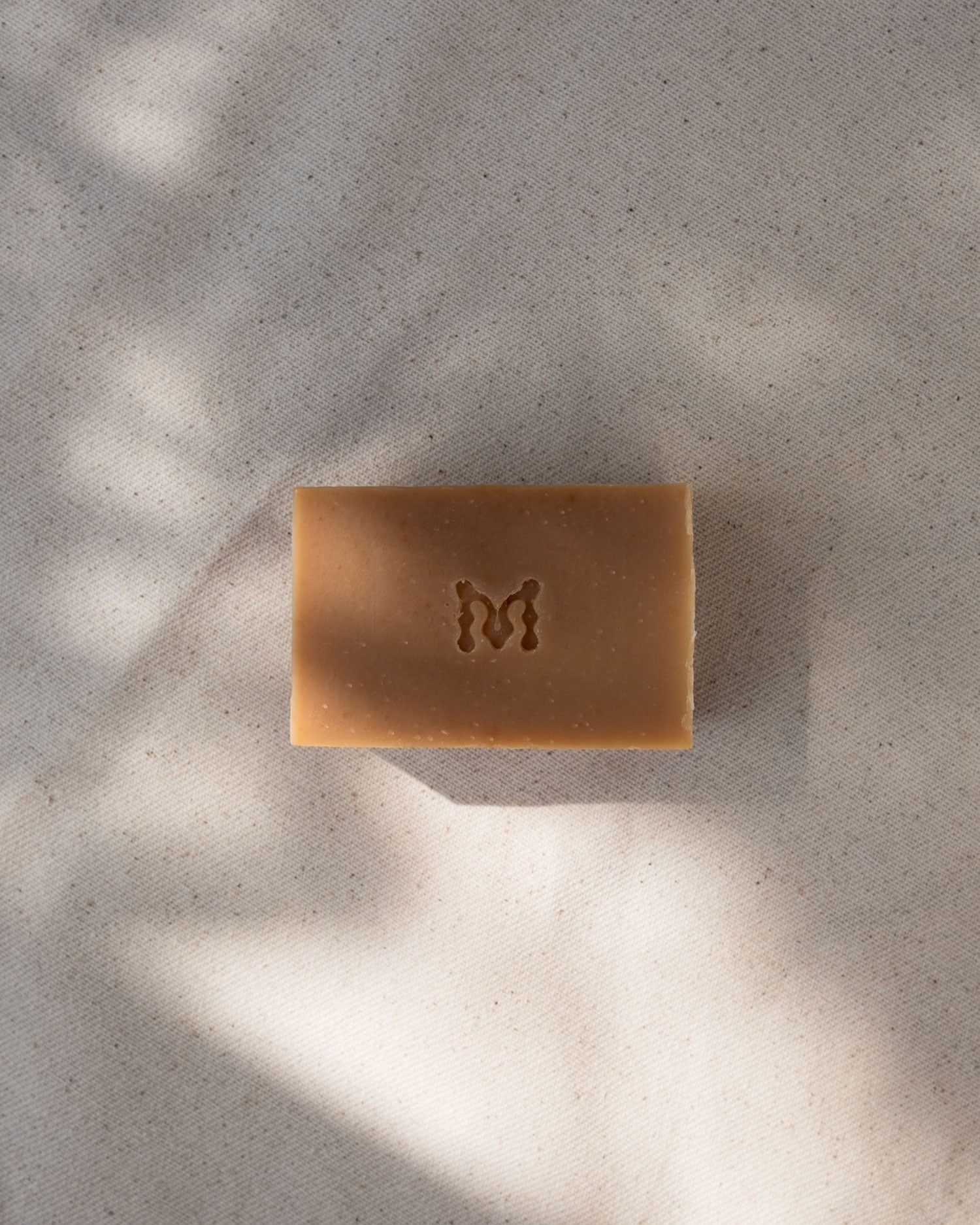 Honey bar of soap with a Momenti logo on a textured surface