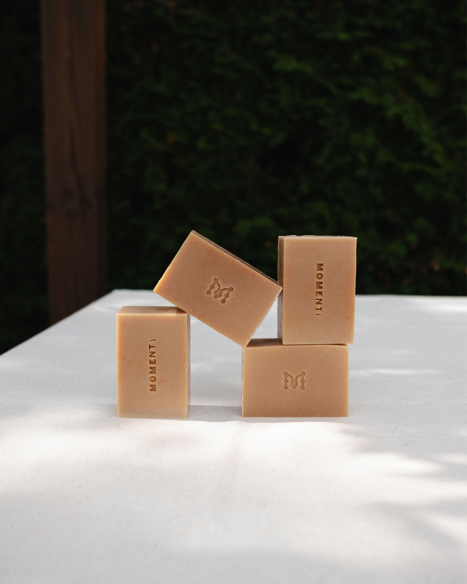 Five beige soap bars with a Momenti logo on a white surface with a dark background