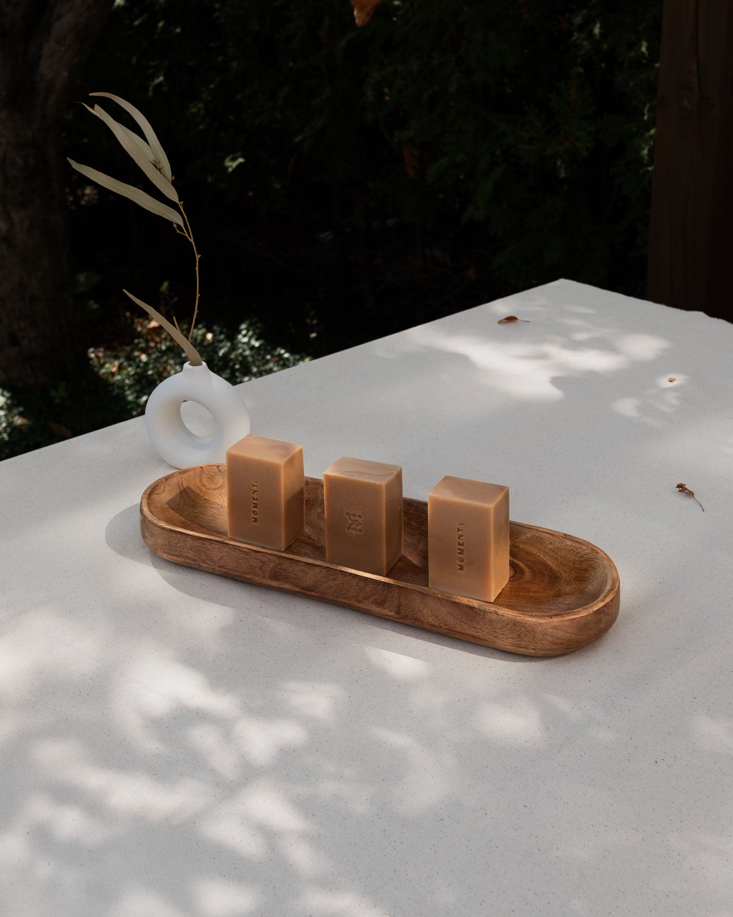 Three honey rectangular bars of soap on a wooden tray with a blurred natural background