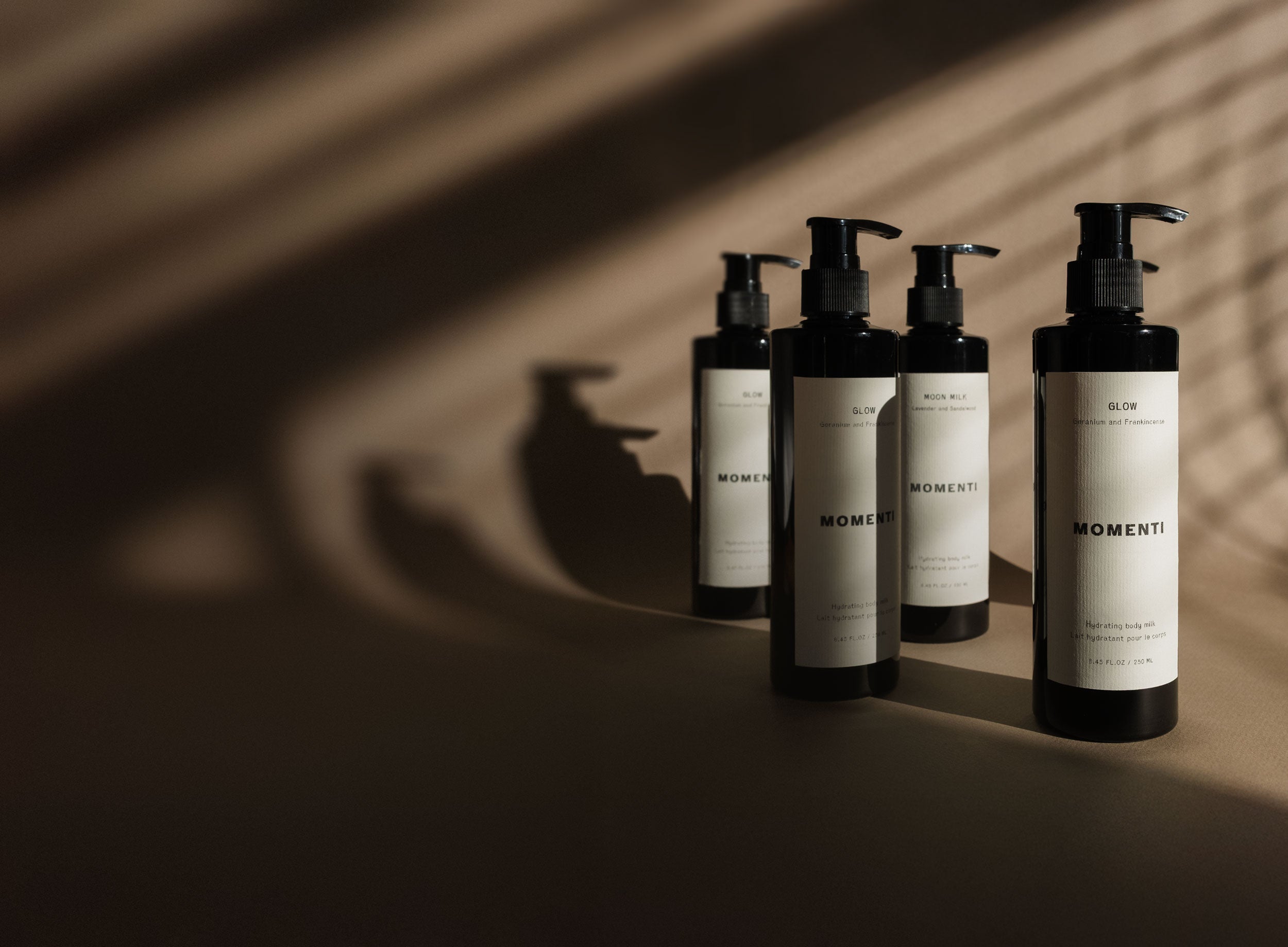 Five hydrating body milk lotions in black bottles with pump dispensers on a brown background