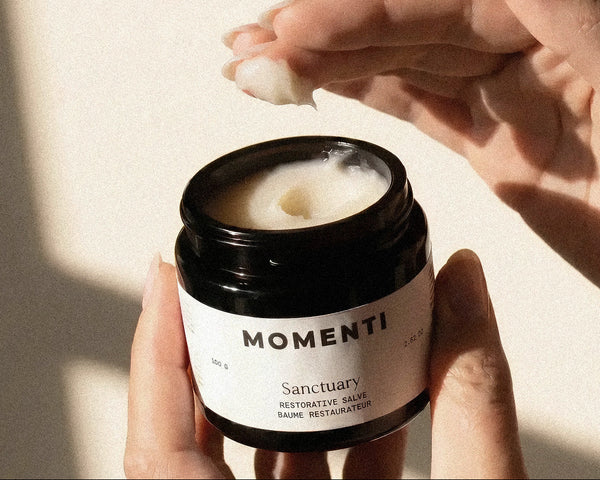 Person applying Momenti Sanctuary restorative salve on a light background