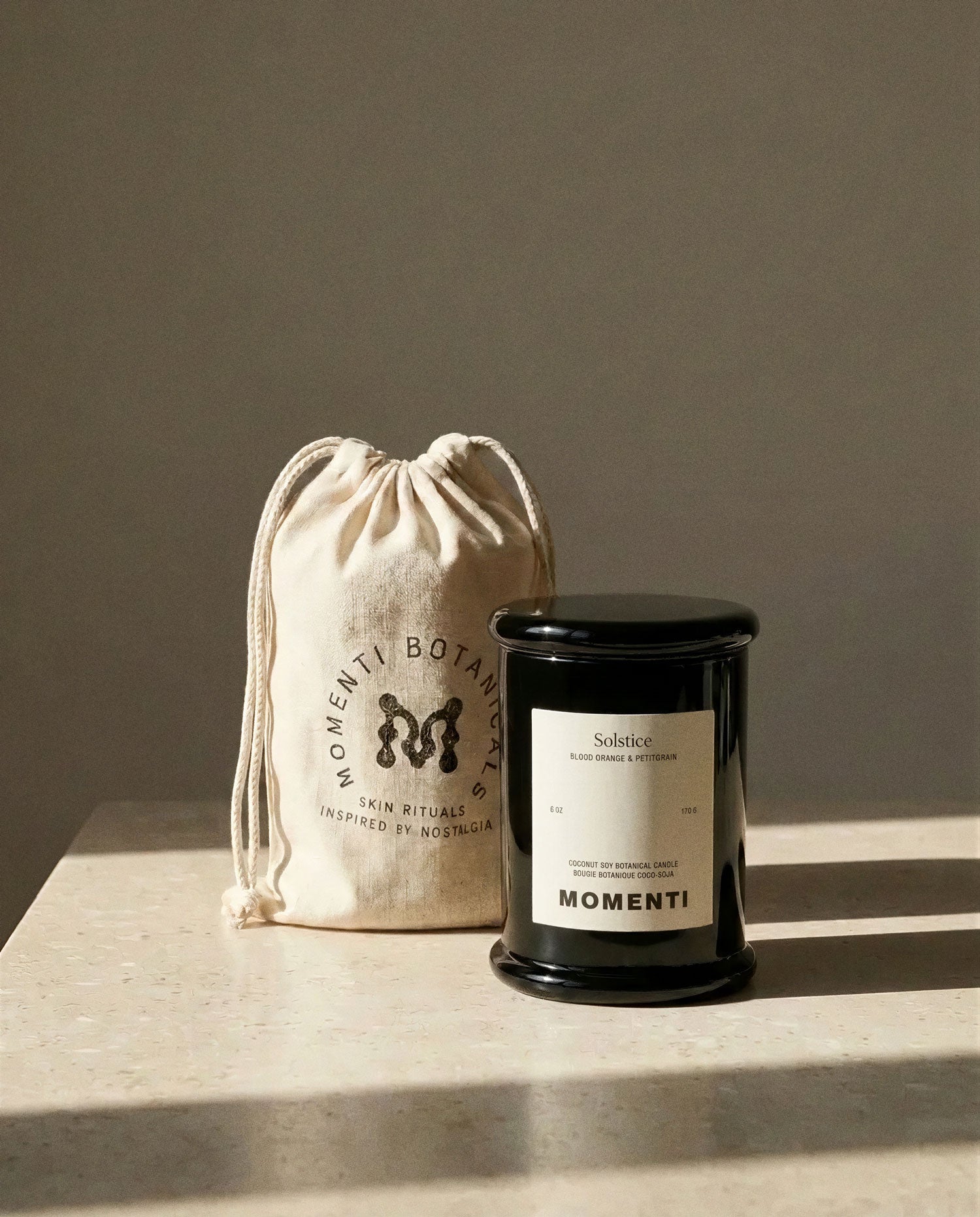 Momenti candle and drawstring bag on a neutral background