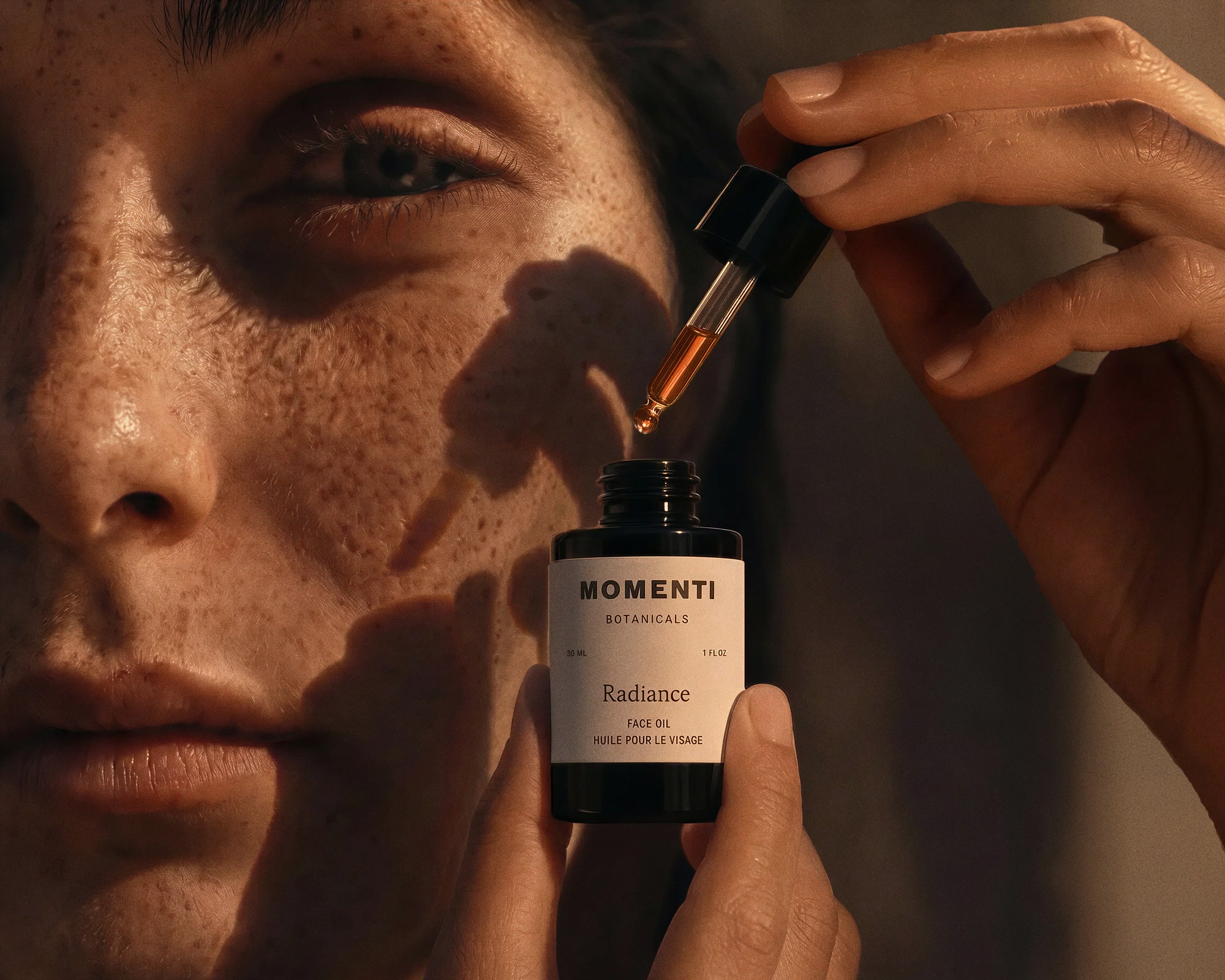 Woman with freckles and natural skin applying Momenti Botanicals Radiance facial oil to their face.