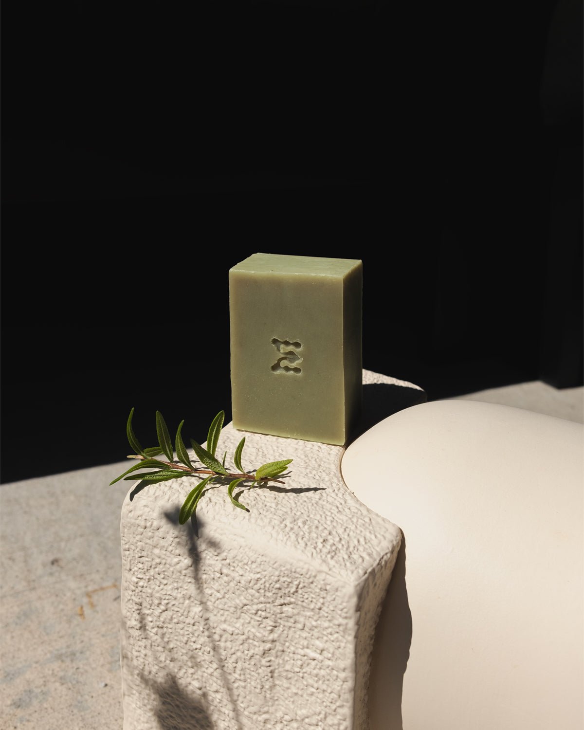 Green rosemary bar of natural soap with a leaf on a stone surface against a dark background
