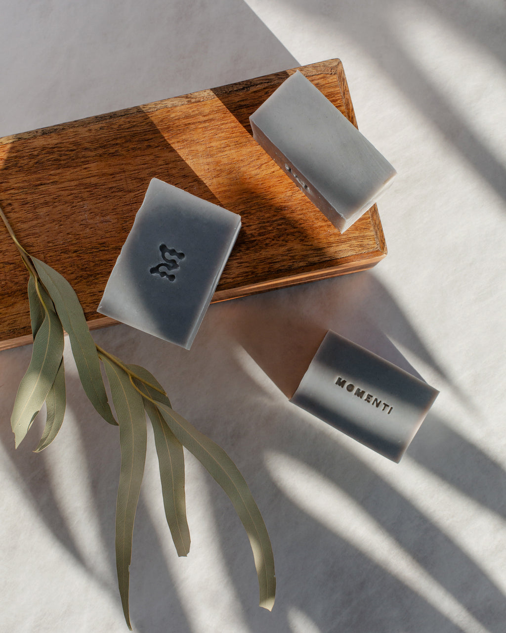 Three bars of soap on a wooden board with a plant leaf on a light background