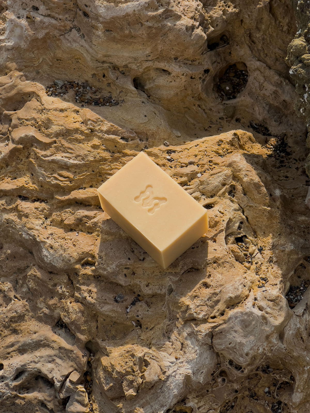 Yellow bar of soap with the Momenti "M" monogram on a beige rocky surface