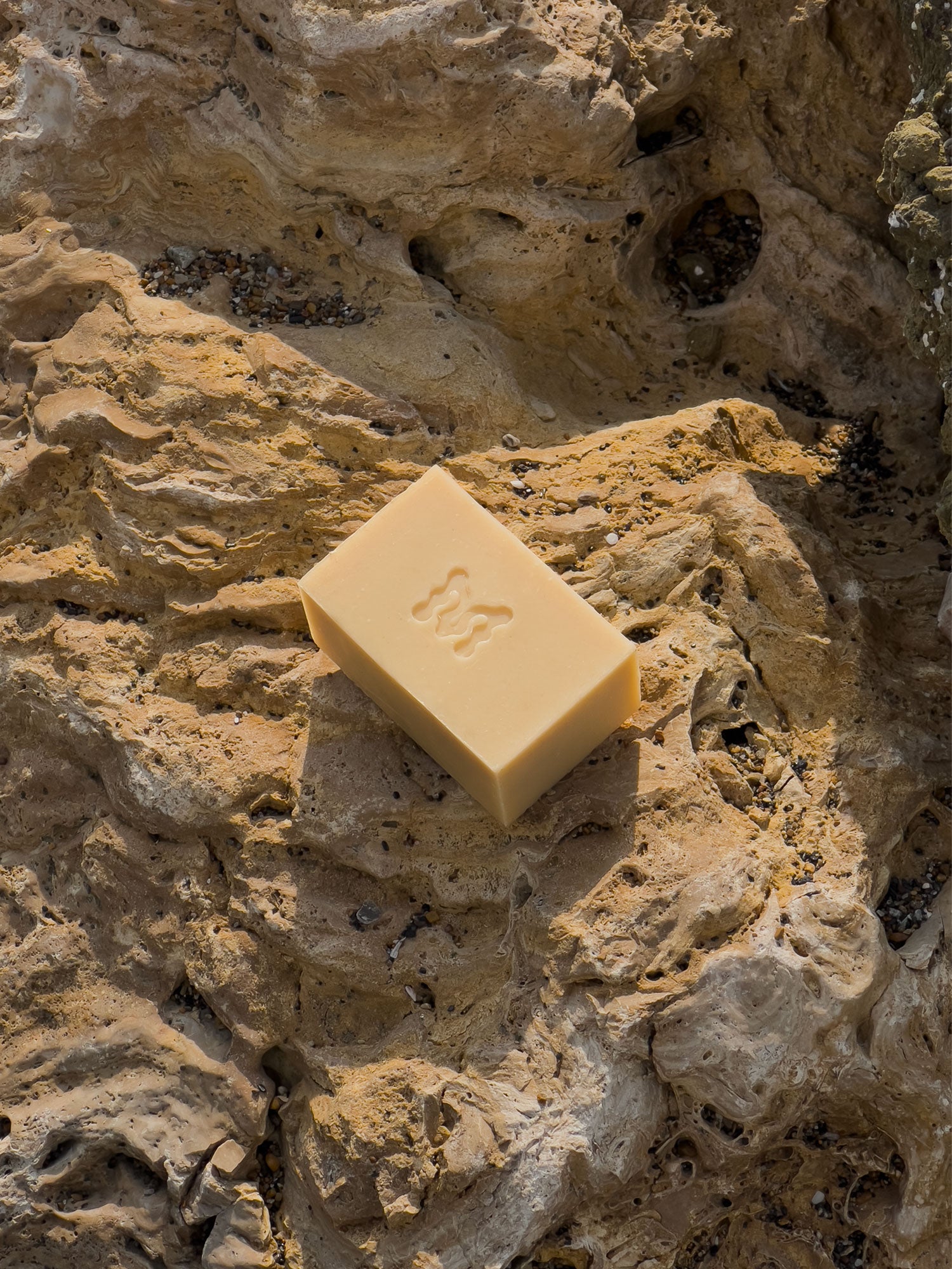 Yellow bar of soap with the Momenti "M" monogram on a beige rocky surface